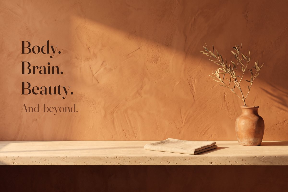 A terracotta plaster wall above a stone ledge with an olive branch in a clay vase, and the words Body. Brain. Beauty. And beyond.